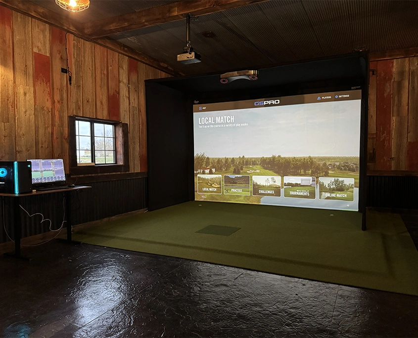 Golf simulator installed in a converted barn with reclaimed wood walls and a projector-mounted impact screen