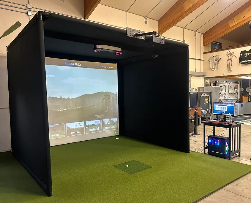 Freestanding golf simulator enclosure with retractable screen and overhead launch monitor installed in a shop space