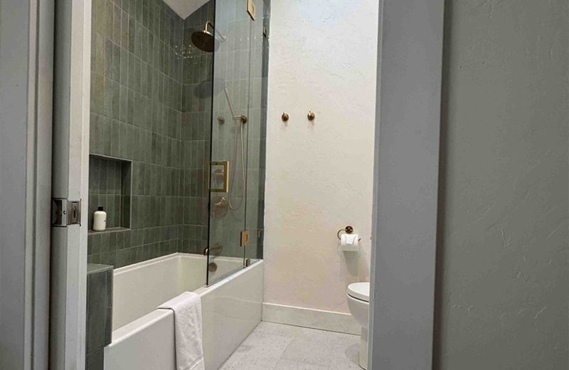 Bathroom remodel with green tile shower and brass fixtures by Upright Build Co.